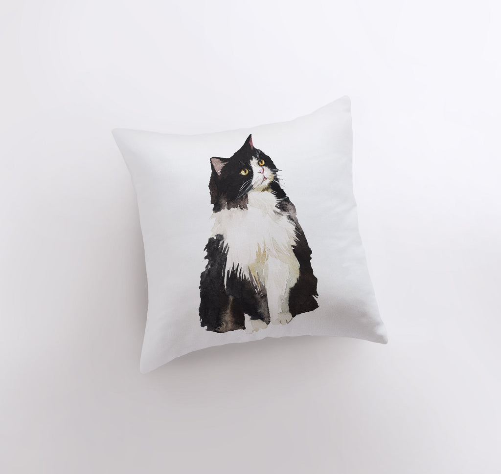 a black and white cat sitting on top of a pillow