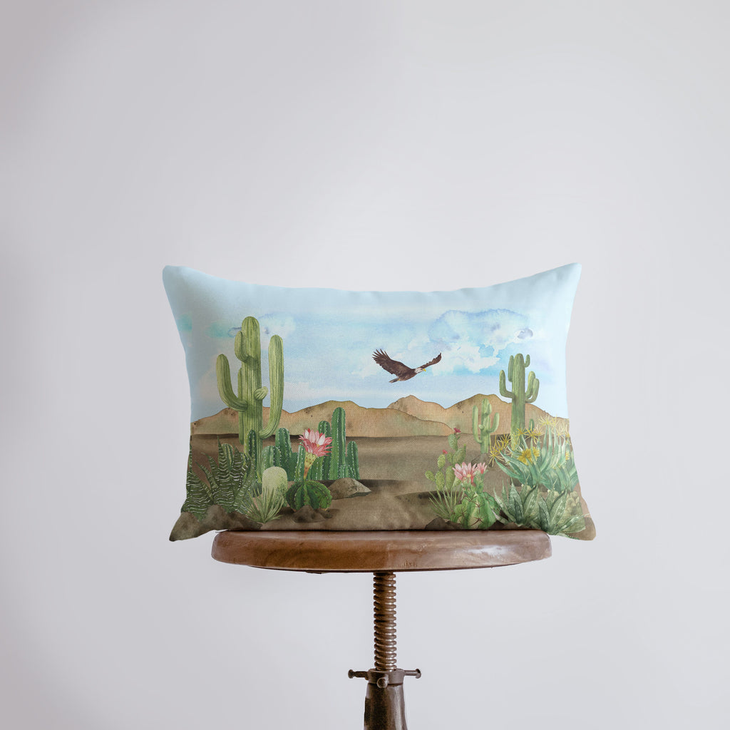 a pillow with a painting of a bird flying over a cactus field