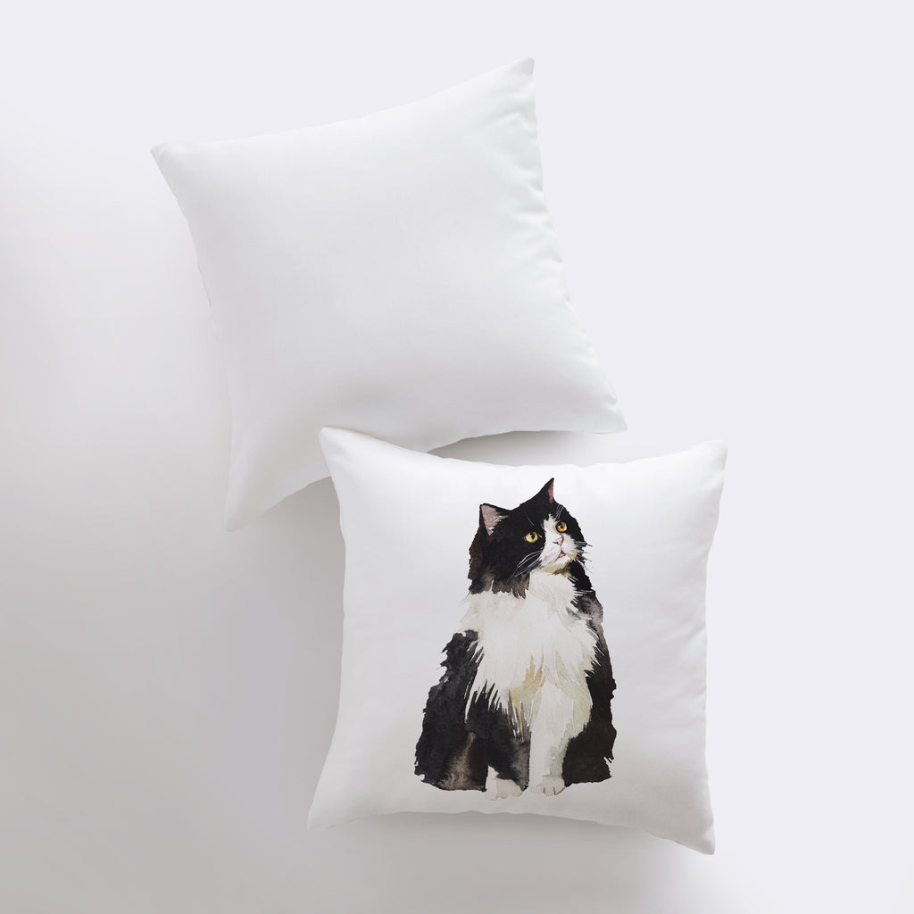 a black and white cat sitting on top of a white pillow