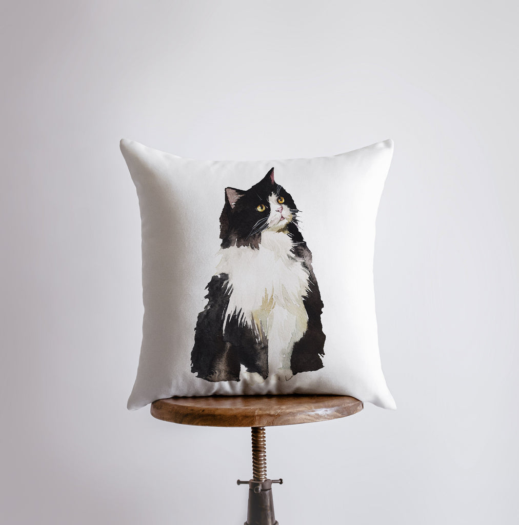 a black and white cat sitting on top of a pillow